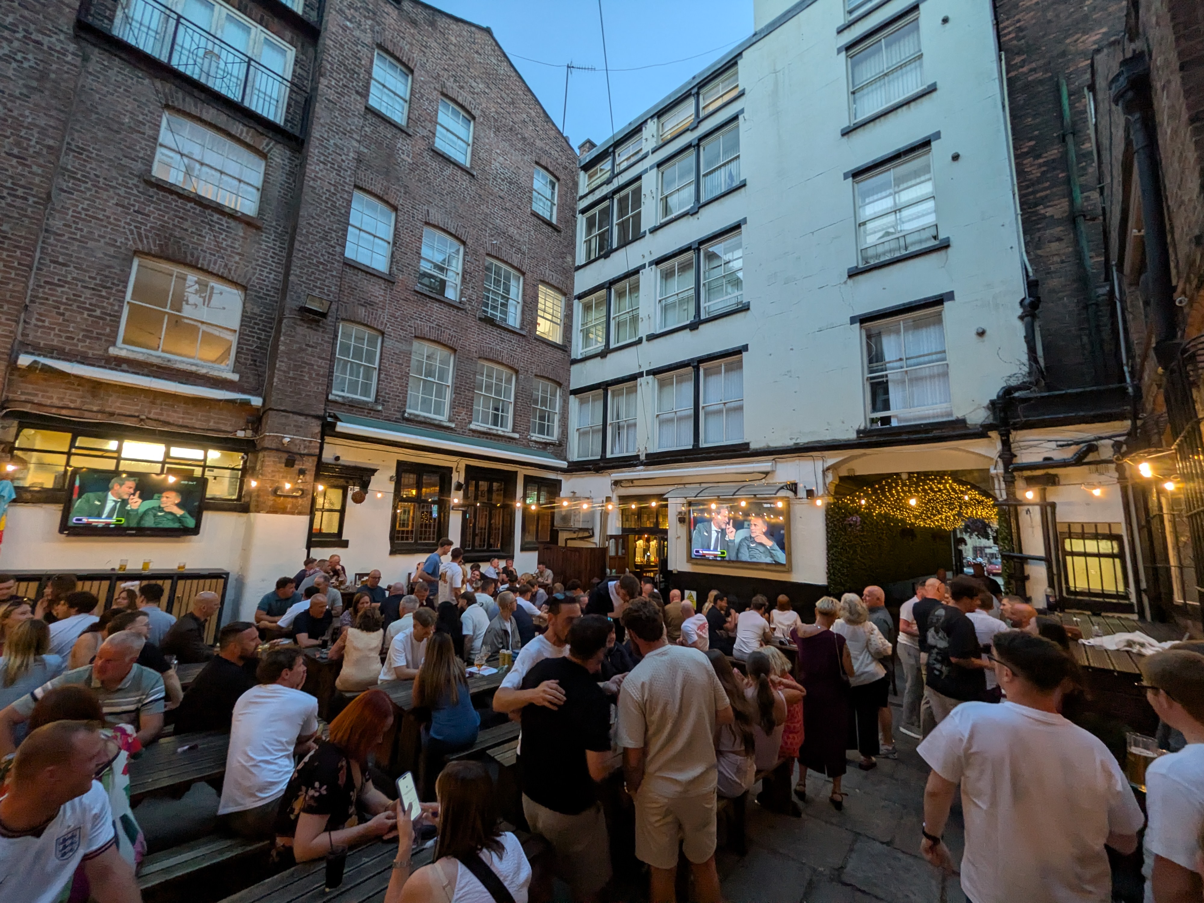 A packed pub courtyard watching England on big screens at dusk