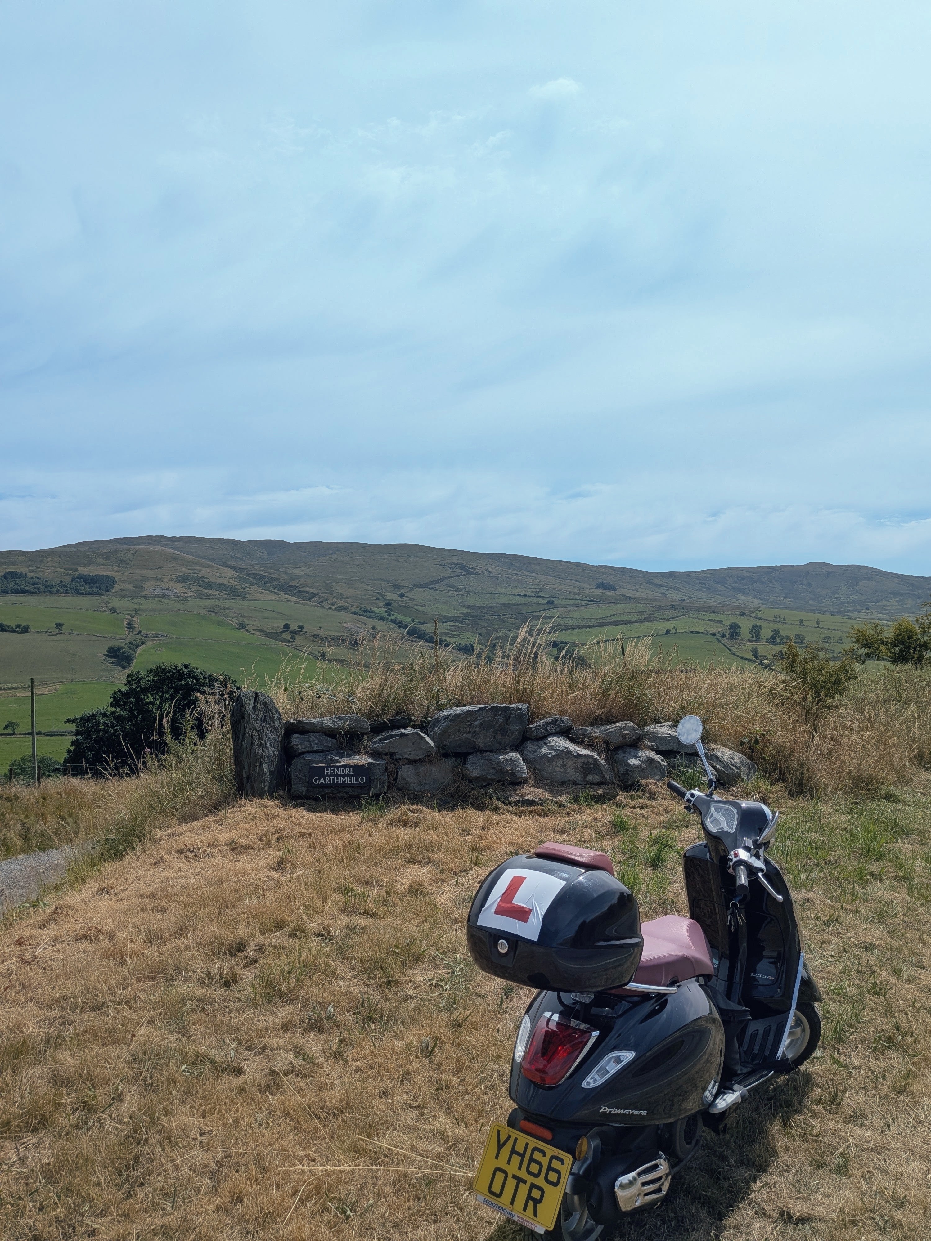 The Vespa parked by a stone wall reading Hendre Garthmeilio, hills beyond