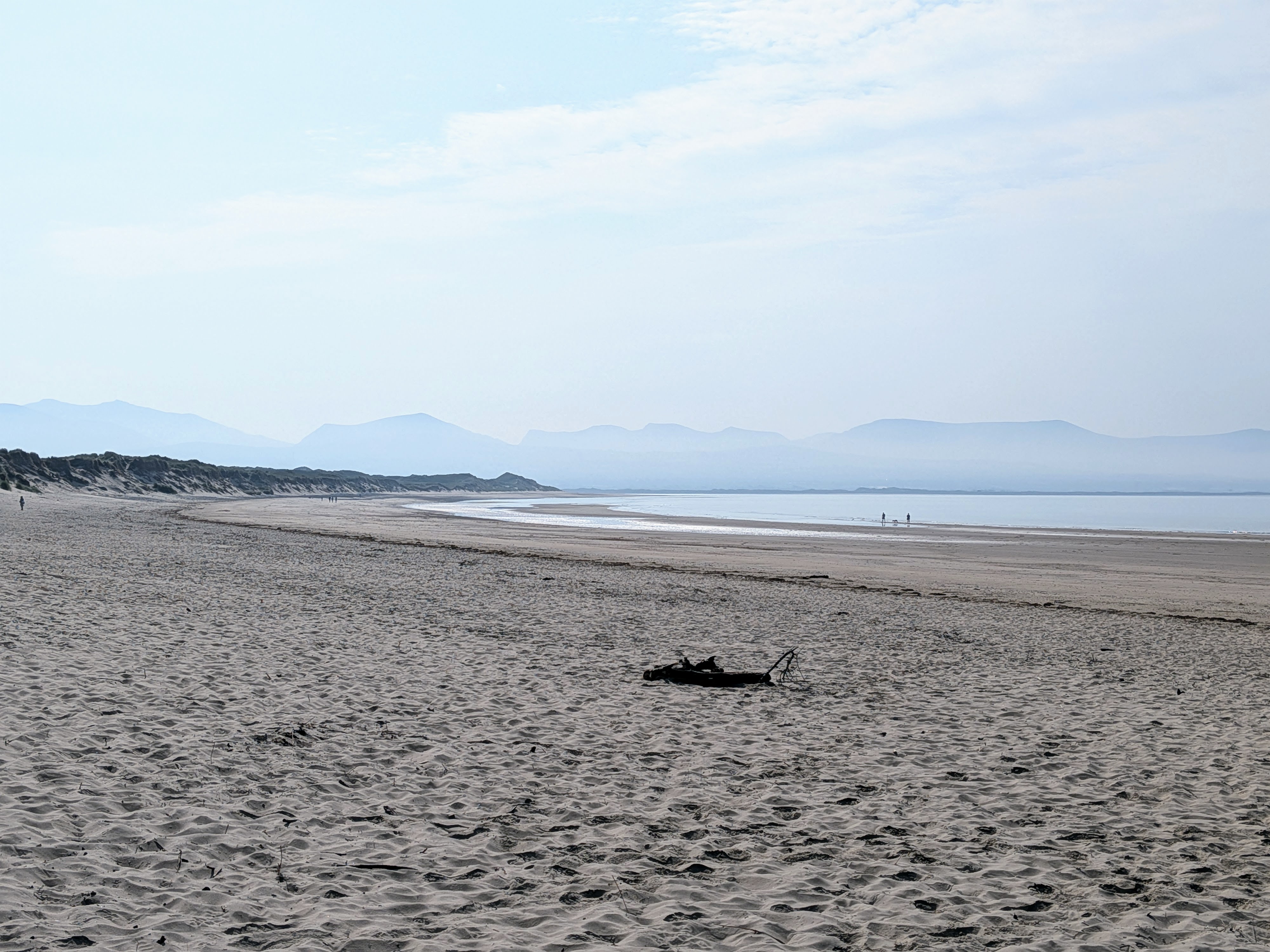 A wide empty Welsh beach at low tide with misty mountains in the distance