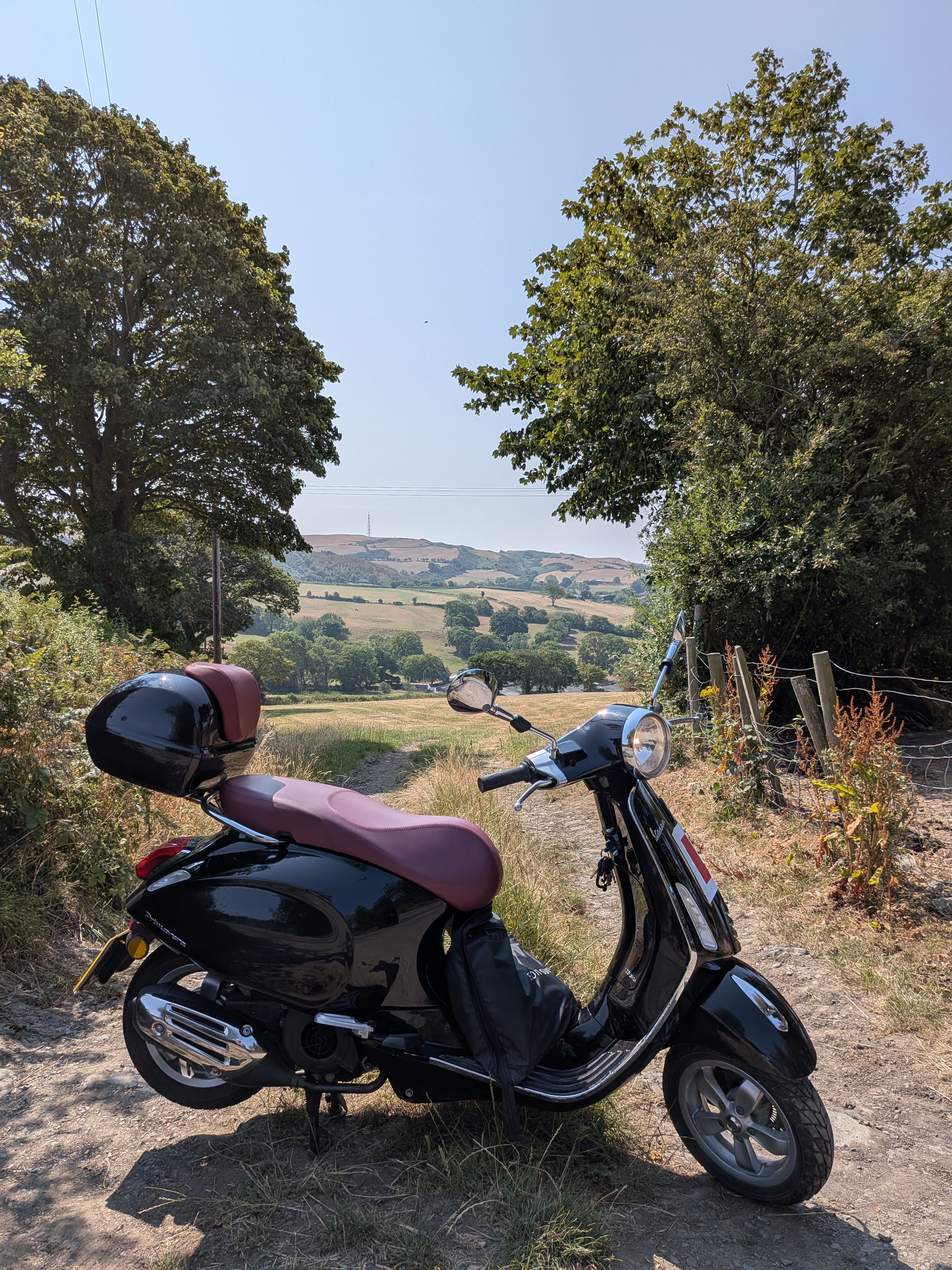 The Vespa parked on a back-lane with rolling Welsh countryside behind